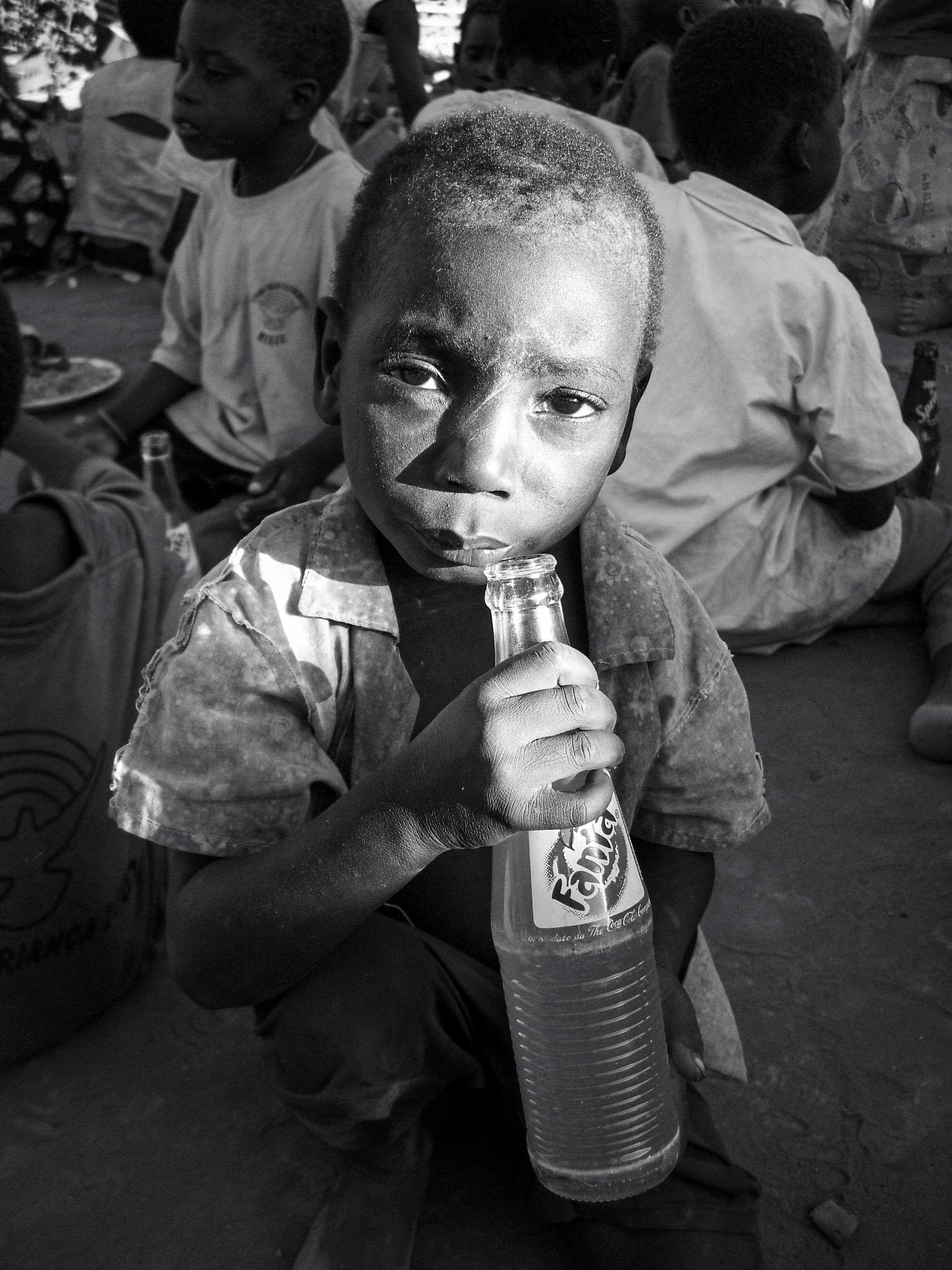 A boy holding a bottle of soda, with other children gathered behind him