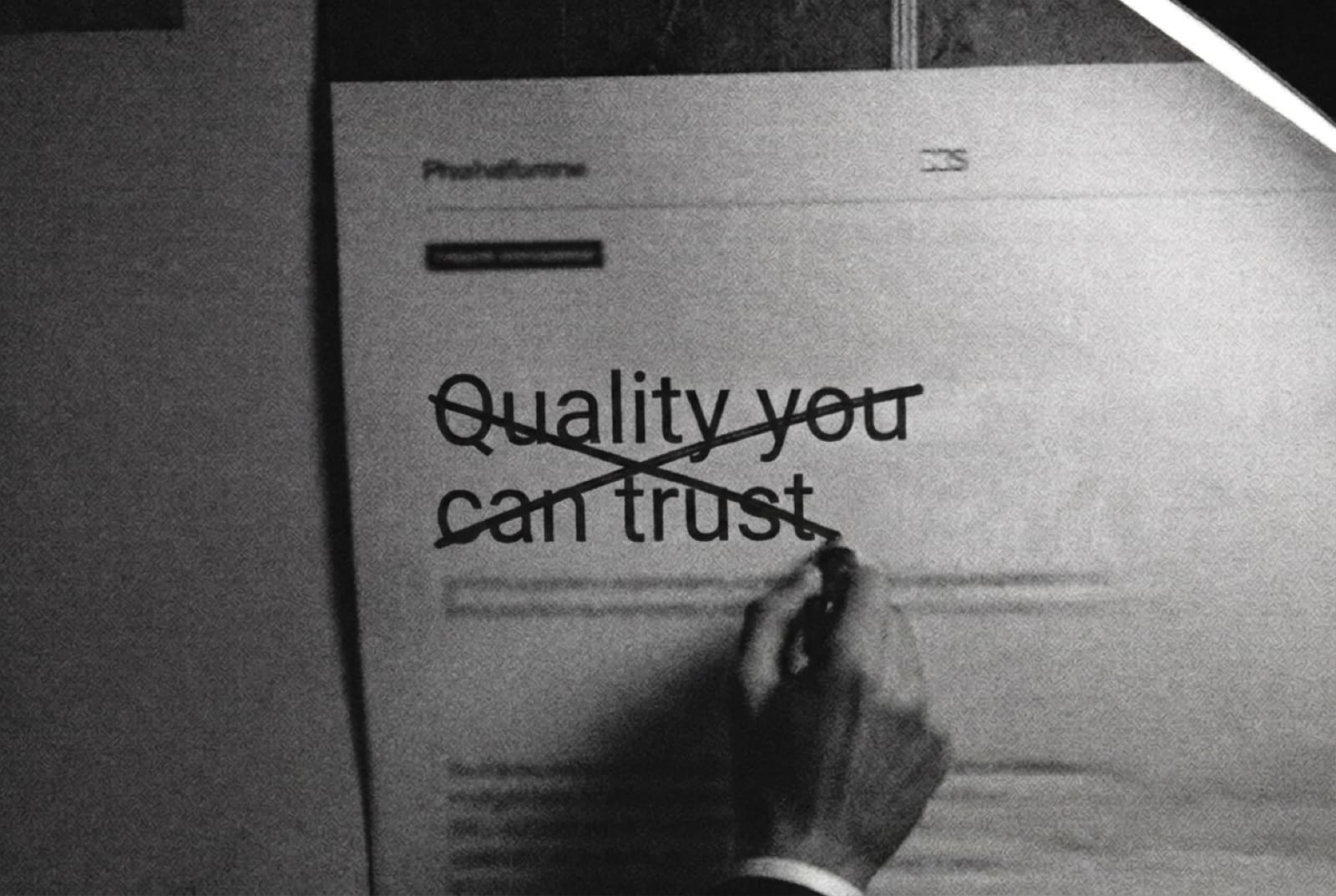 A hand striking through the printed headline 'Quality you can trust.' with a marker under a work lamp