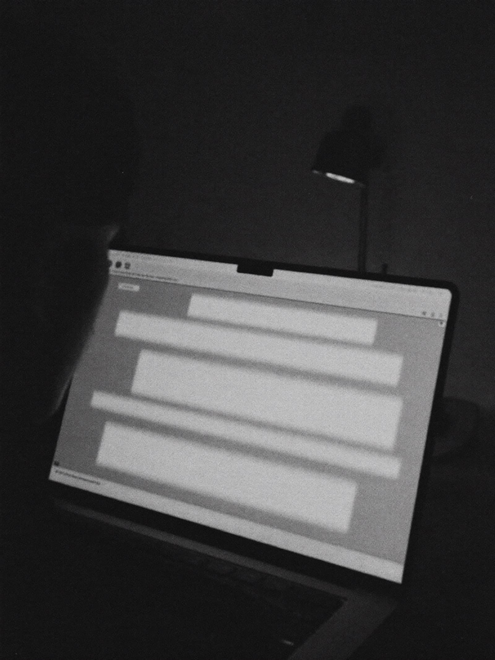 Over the shoulder of someone scrolling a glowing webpage on a laptop in a dark room