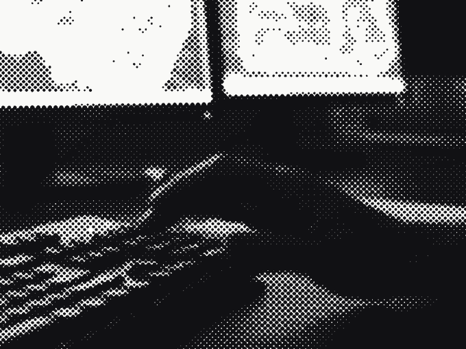 Hands working a keyboard between two monitors of technical drawings, a build in progress