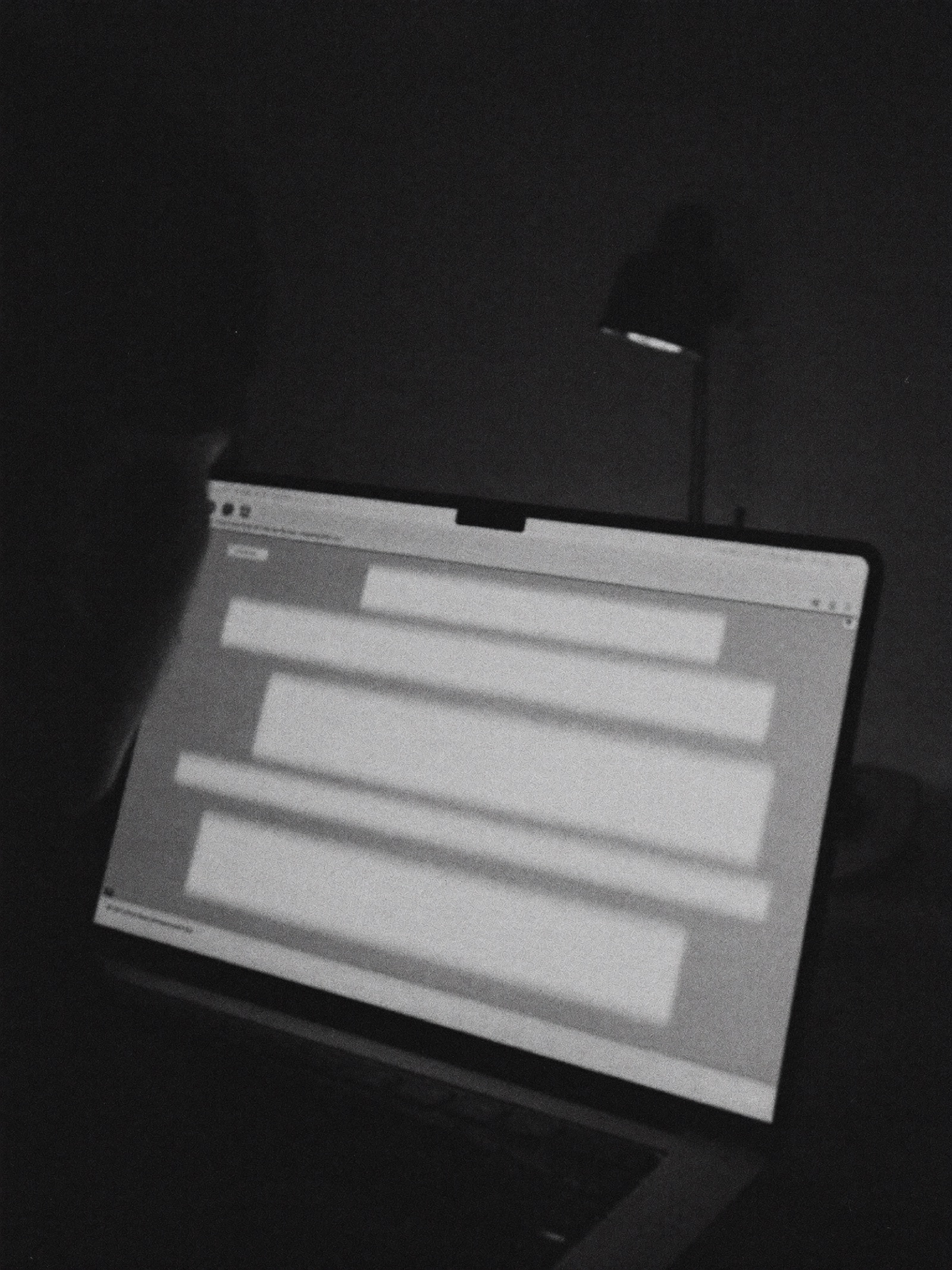 Over the shoulder of someone scrolling a glowing webpage on a laptop in a dark room